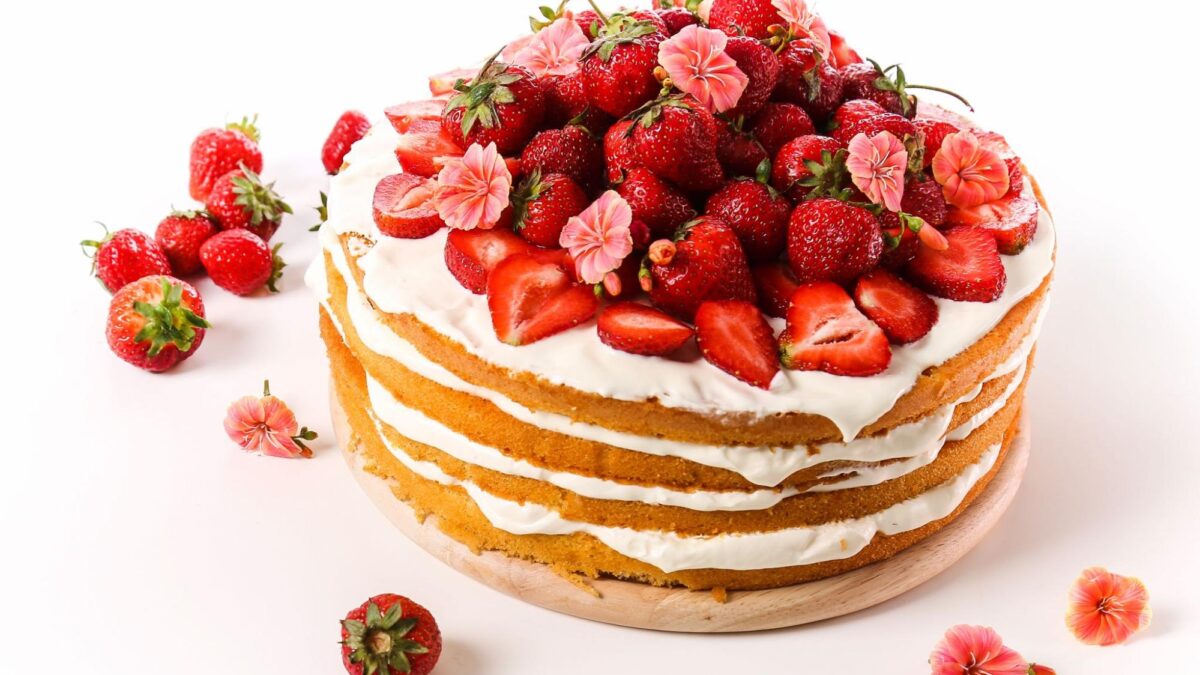 a four-layer strawberry cream cake with a few strawberries around it