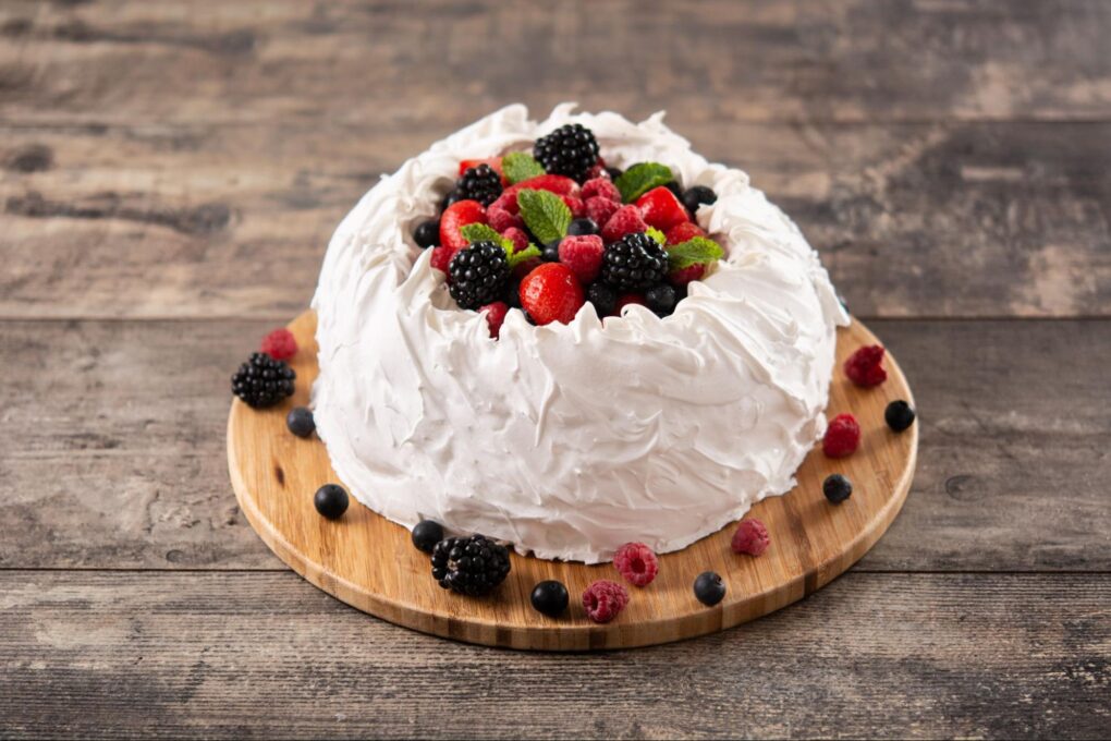 A cake with white frosting and berries on a wooden tray