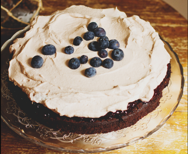 A cake with whipped cream abnd blueberries on a glass plate