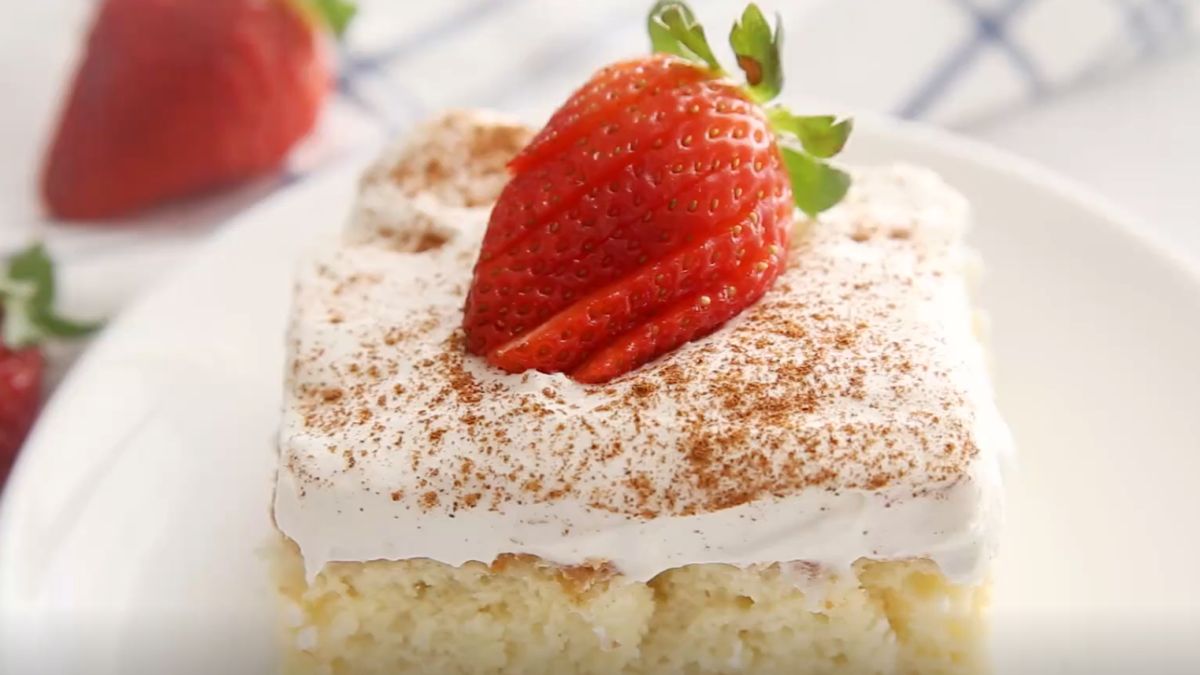 A piece of tres leches cake with cream and a strawberry on top