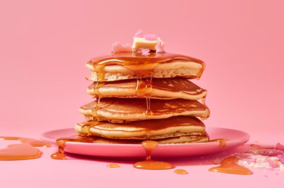 five thick pancakes with maple syrup on a pink background