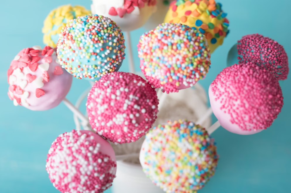 different pop cakes with sprinkles in a white glass on a light blue background